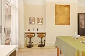 A room with a dining table set for two, a bar area with stools, and a large abstract painting on the wall.