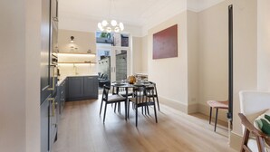Una cocina moderna con armarios oscuros y una isla central, un área de comedor con una mesa redonda y sillas, y un amplio ventanal que proporciona luz natural.