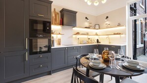 Una cocina moderna con armarios oscuros, horno empotrado y comedor preparado para seis personas, con una mesa redonda y sillas.