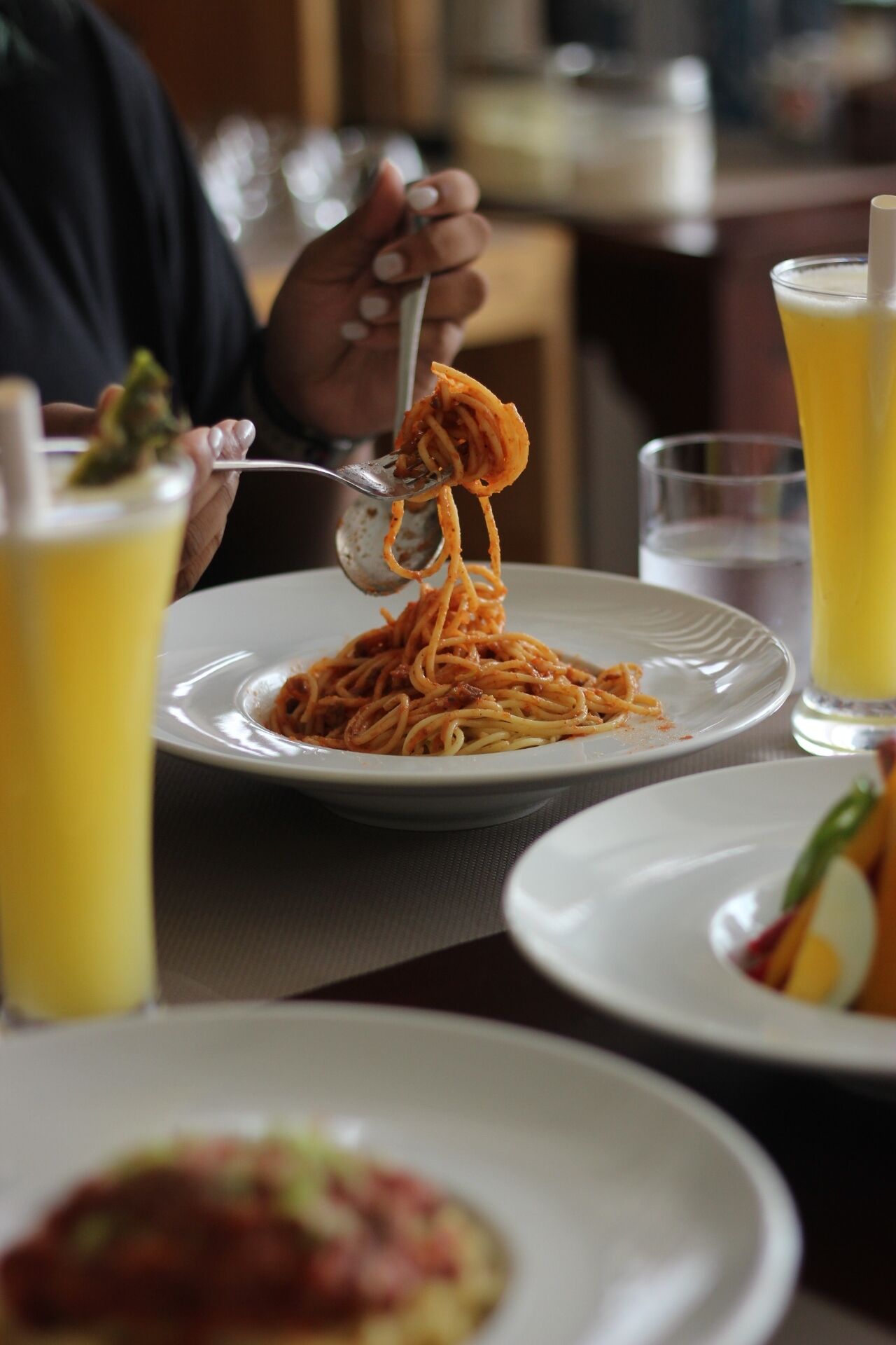 Uma mesa de jantar com um prato de espaguete e um copo de suco de laranja.