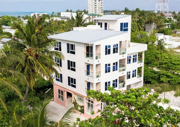 A multi-story hotel with balconies, surrounded by lush greenery and a view of the sea. - Blissview Maldives (Thulusdhoo Island)