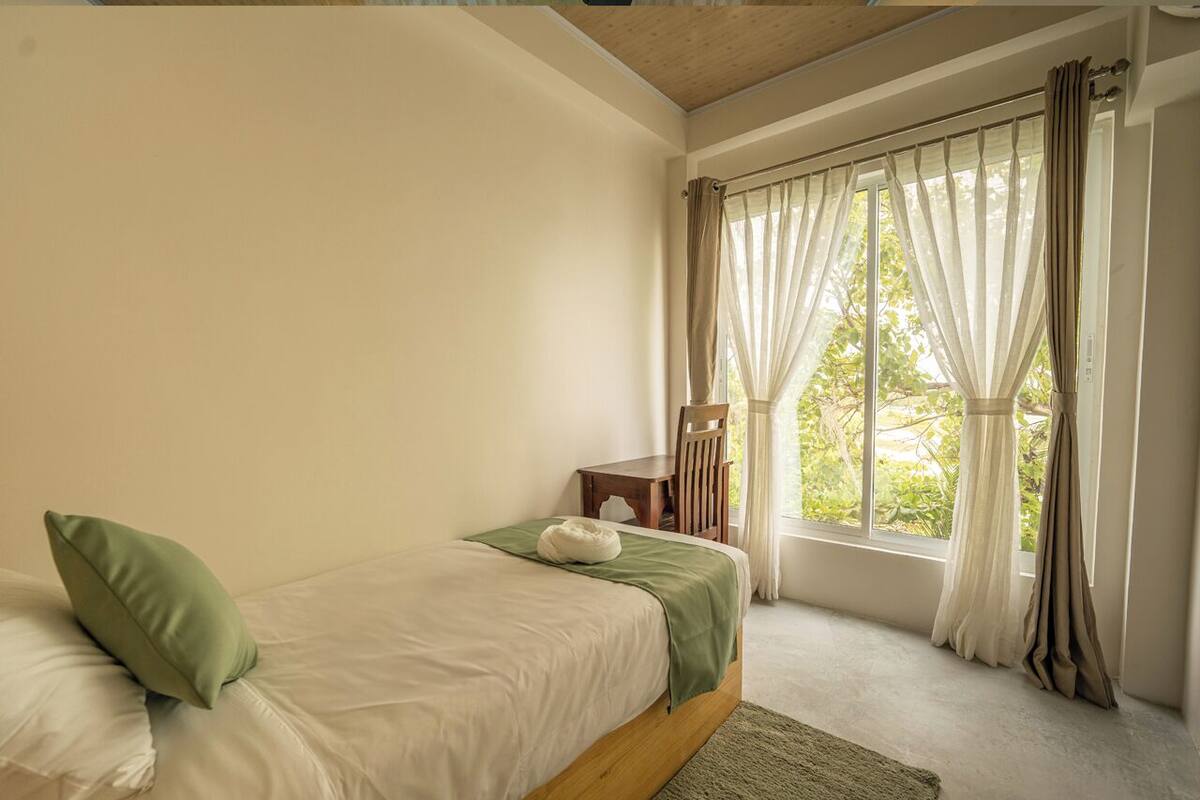 A bedroom with a single bed, a nightstand, a chair, and a window with curtains.