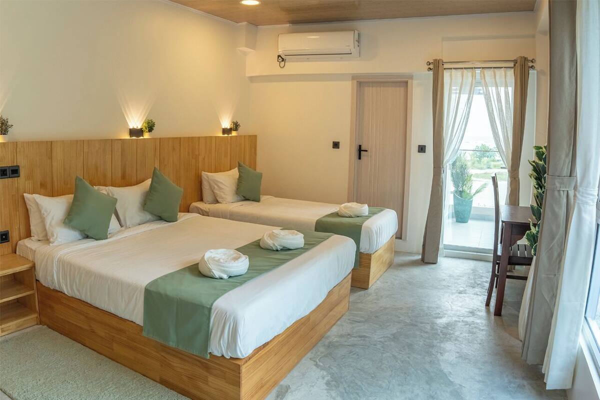 A hotel room with two wooden beds, a small table, and a door leading to a balcony.