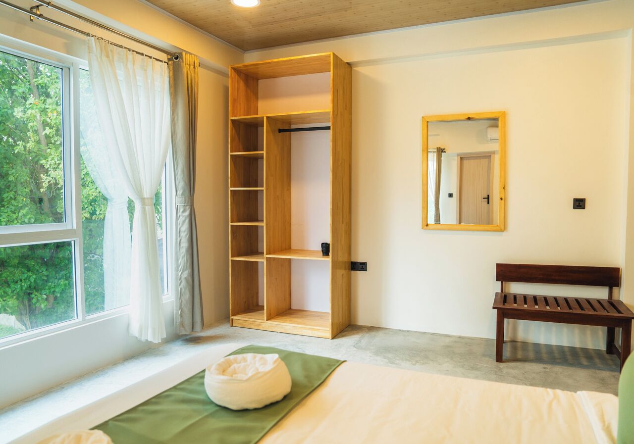 Une chambre à coucher avec une armoire en bois, un banc, un lit et une fenêtre avec des rideaux.