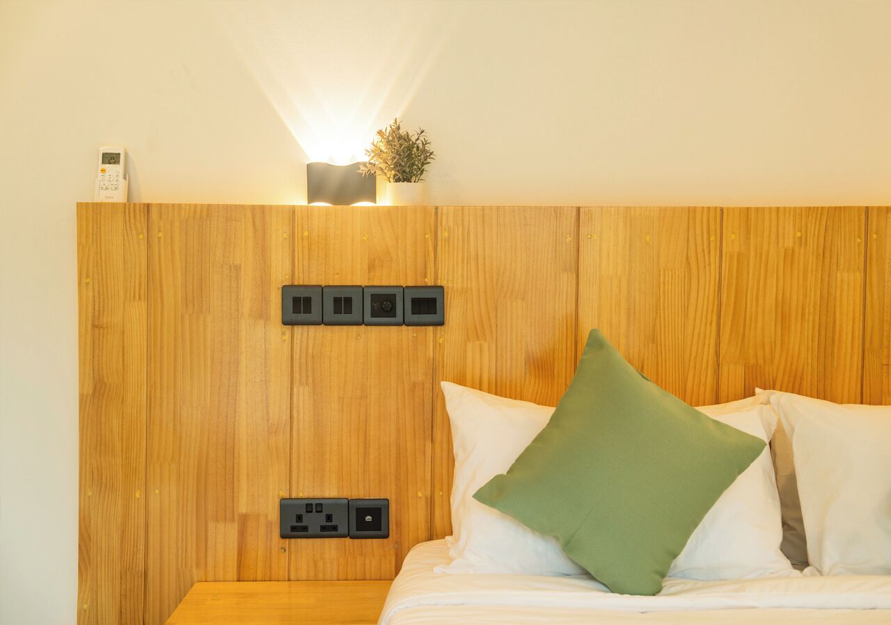 A hotel room with a wooden headboard, a bedside table with a lamp, and a green pillow.
