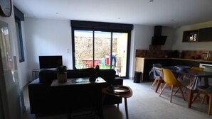 A modern living room with a sofa, a dining table with chairs, and a kitchen area with a microwave. - Country house in Brière, 20 minutes from the beach. (Donges)