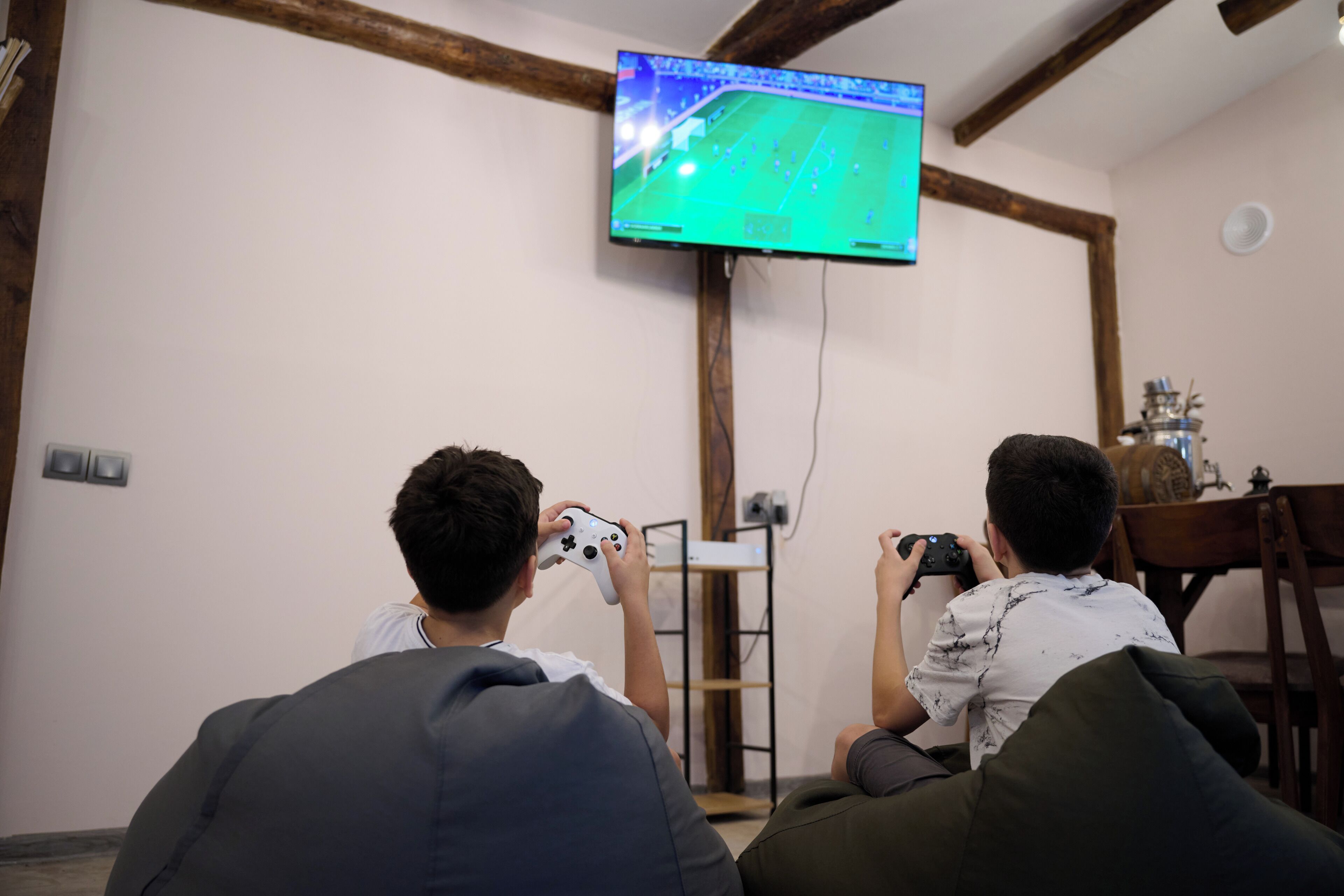 Zwei Personen sitzen auf einer Couch und spielen ein Videospiel, während ein Fernseher an der Wand hängt.