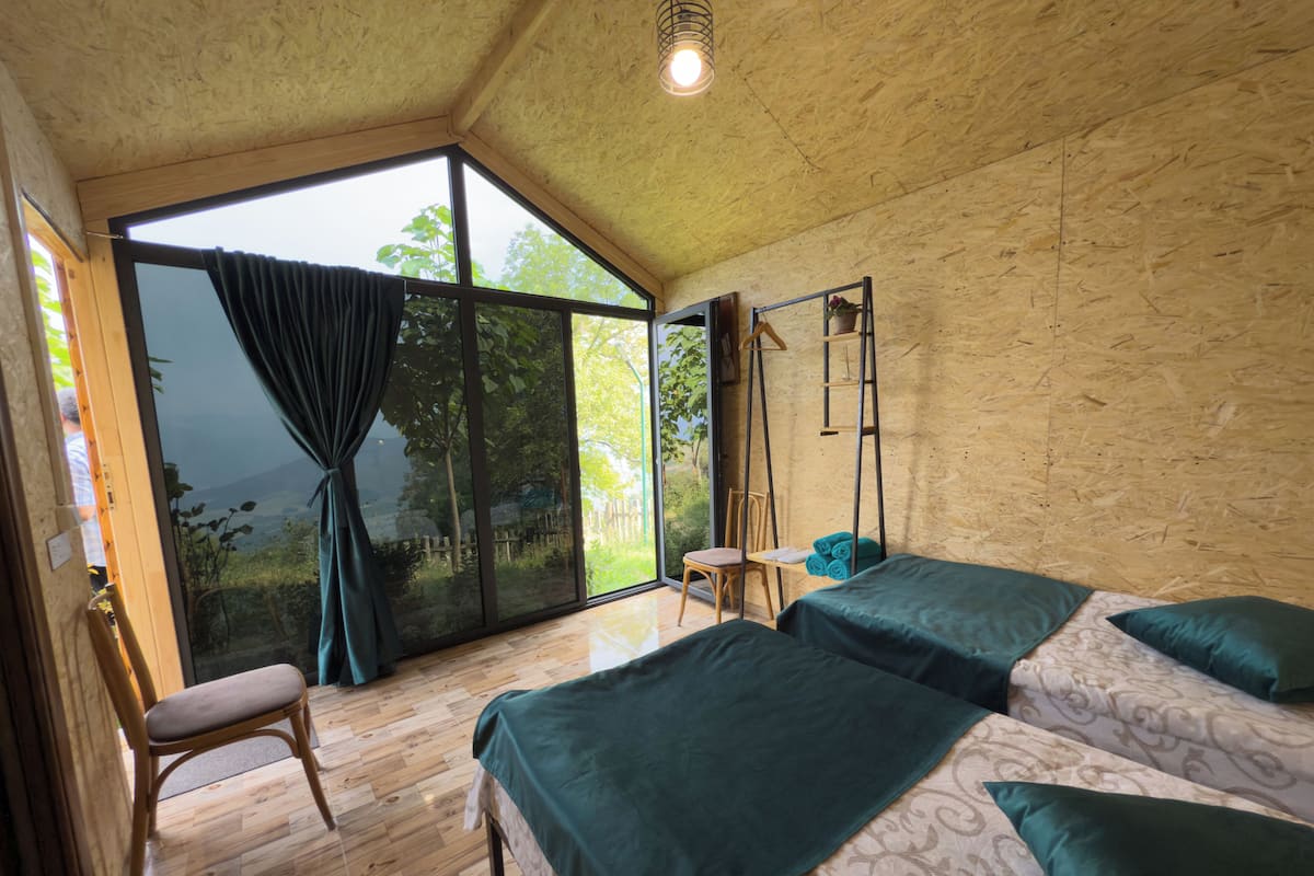 A room with two beds, a chair, a small table, and a large window with curtains.