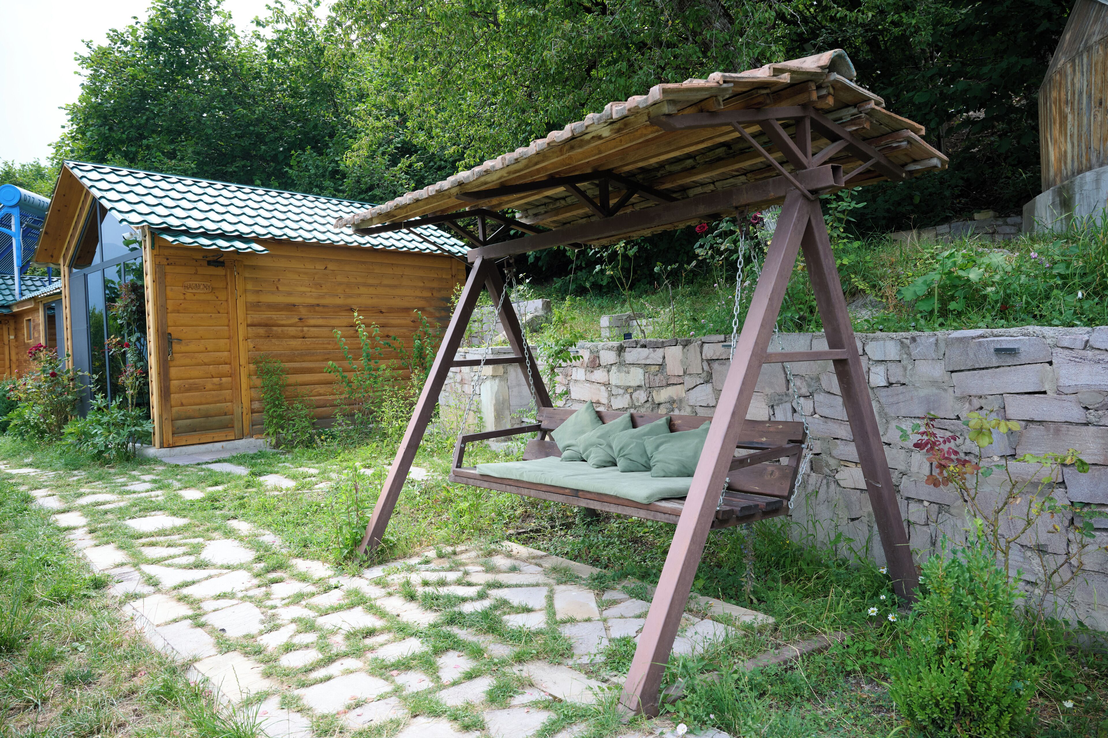A wooden swing with a metal frame, a small wooden shed, and a stone wall.
