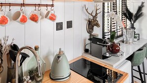 Una cocina con microondas, hervidor y diversos utensilios de cocina. También hay elementos decorativos como una cabeza de venado y flores sobre la encimera.