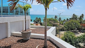 A rooftop terrace with two potted palm trees, pebbles, and a view of the ocean. - Conforto e localização Nixxus I (Ipojuca)