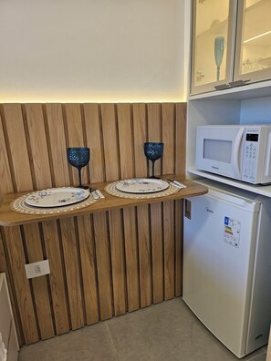 Compact kitchenette with refrigerator, microwave, and glassware holders.