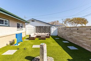 A backyard with artificial grass, a wooden fence, a sofa set, and a decorative wall.