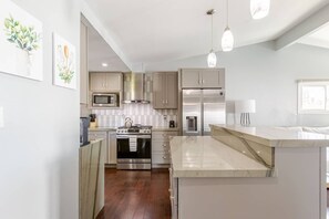 Una cocina moderna con electrodomésticos de acero inoxidable, encimera de mármol e iluminación colgante.