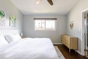 Un dormitorio con cama, cómoda de madera, ventana con vistas y ventilador de techo.