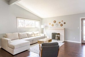 A living room with a sectional sofa, a coffee table, a fireplace, and a large window.