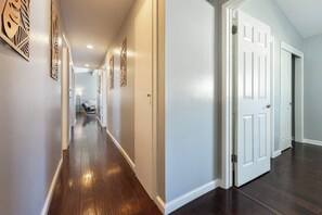 Un pasillo con piso de madera y paredes blancas que conduce a varias puertas blancas.