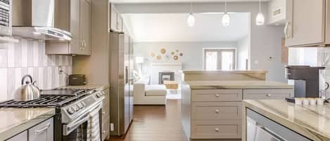 A modern kitchen with stainless steel appliances, wooden flooring, and pendant lighting.
