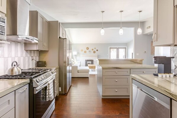 A modern kitchen with stainless steel appliances, wooden flooring, and pendant lighting.
