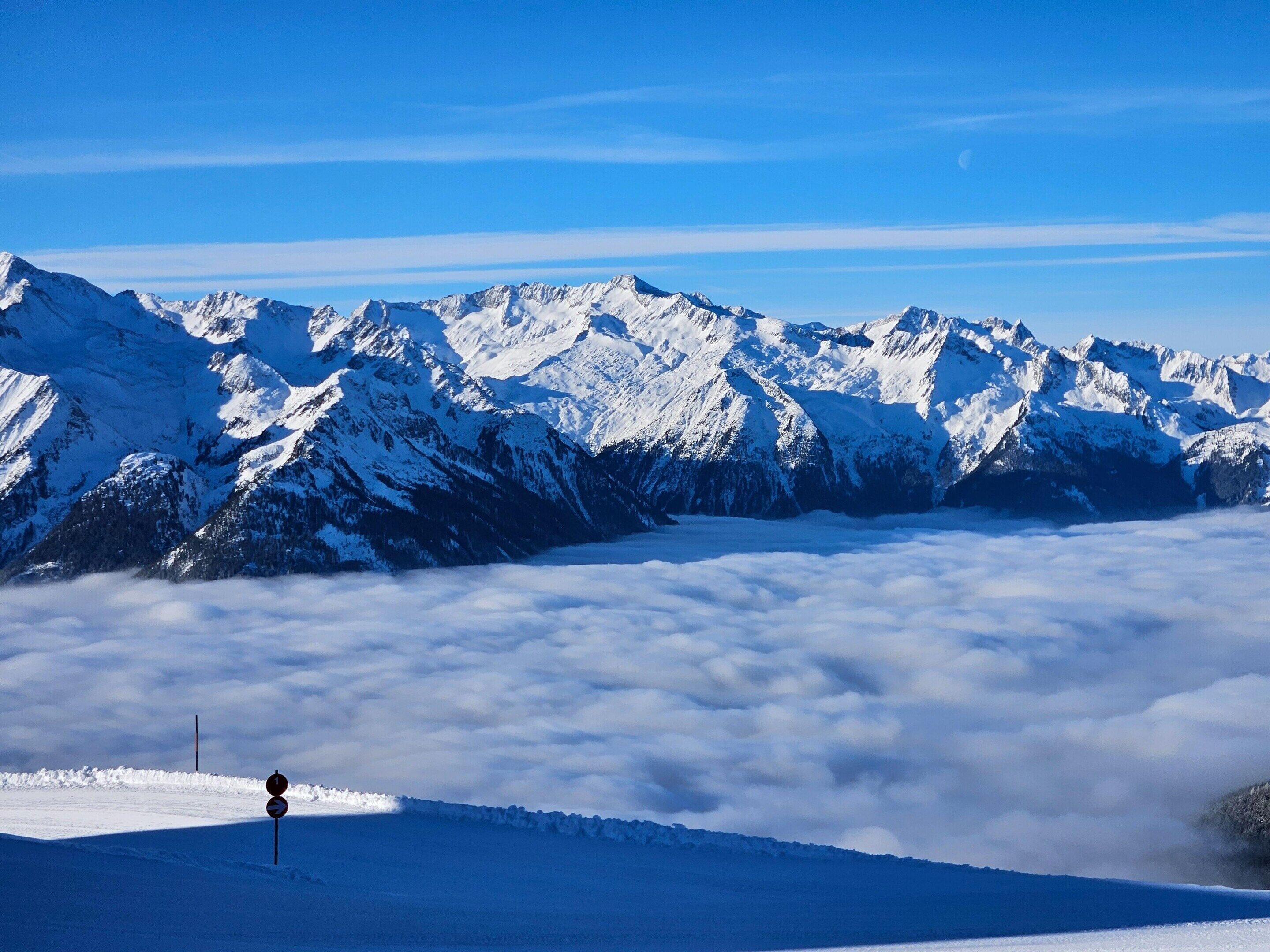 A snow-covered mountain range with a clear sky and a road sign in the foreground.