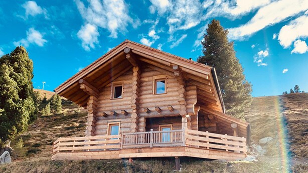 Eine Holzhütte mit Balkon, gelegen an einem Hang unter blauem Himmel.