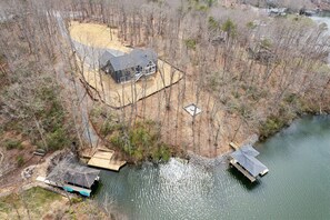 An aerial view of a house with a dock and a boat, surrounded by trees and a body of water.