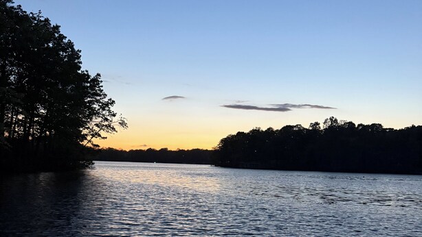Een rustig meer bij zonsondergang, met een houten steiger op de voorgrond.