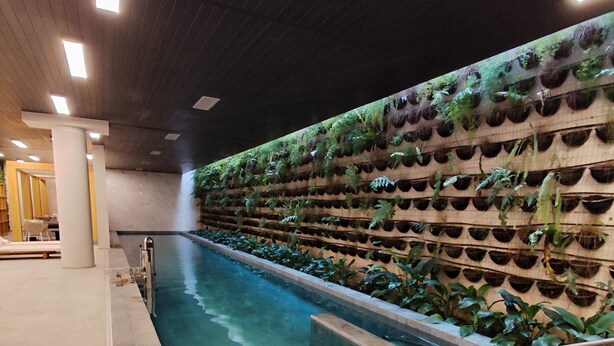 A swimming pool with a tiled edge, a wall of planters, and a ceiling with recessed lighting.