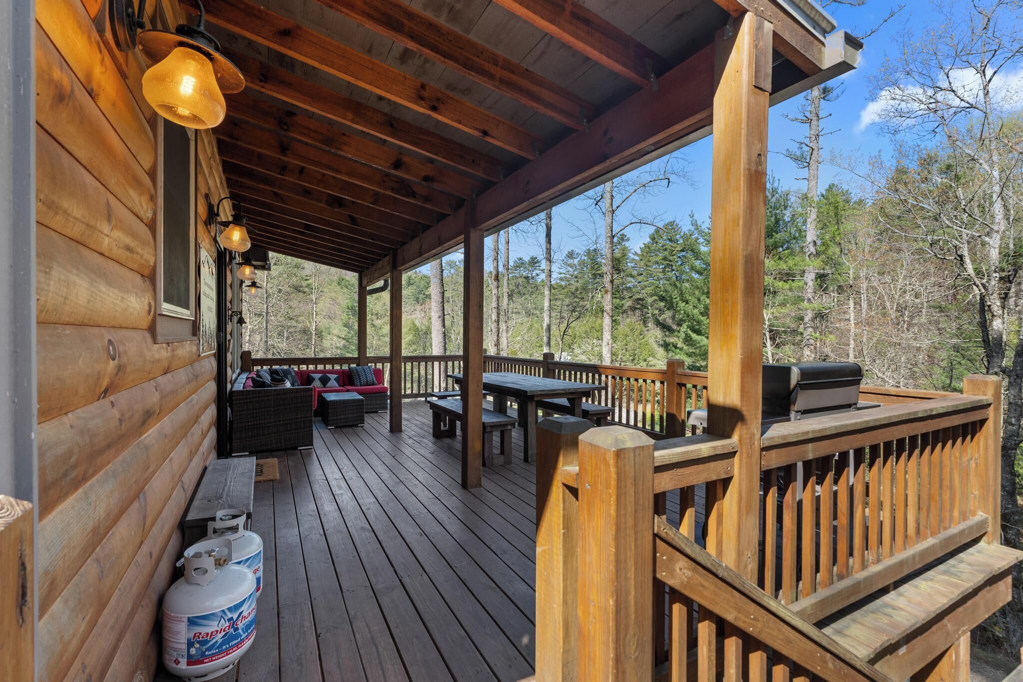 A wooden deck with outdoor seating, a grill, and a propane tank.