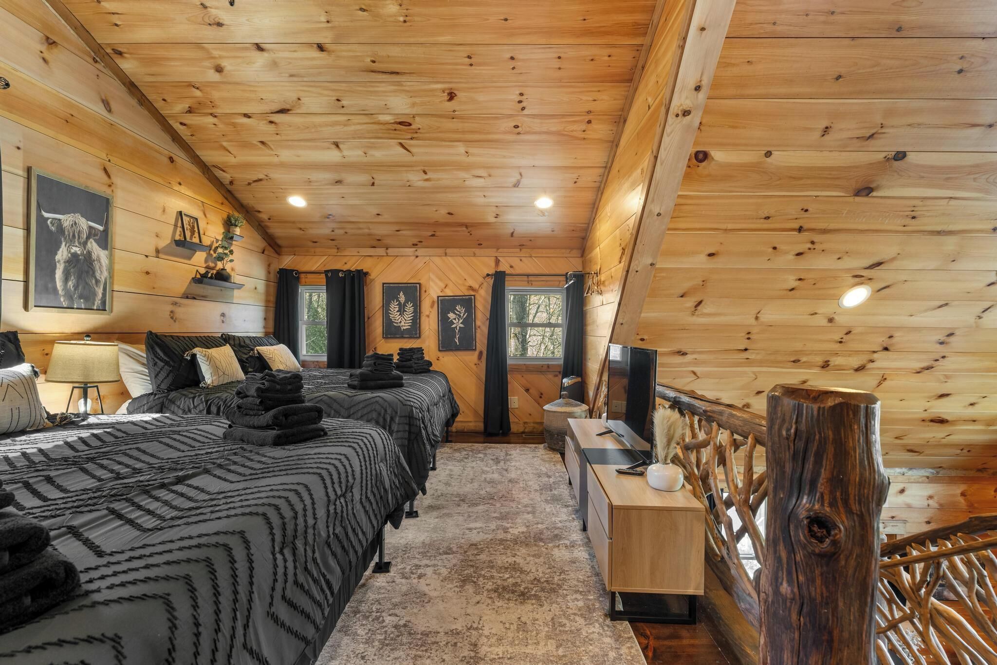 A wooden cabin bedroom with two beds, a desk, and a TV.