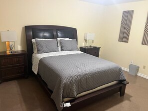 A neatly made bed with a grey quilt, two bedside tables with lamps, and a wall with abstract art. - Level up lounge home. Great family retreat! (McAllen)