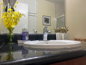 A bathroom sink with a mirror, a vase of yellow flowers, and toiletries. - Level up lounge home. Great family retreat! (McAllen)