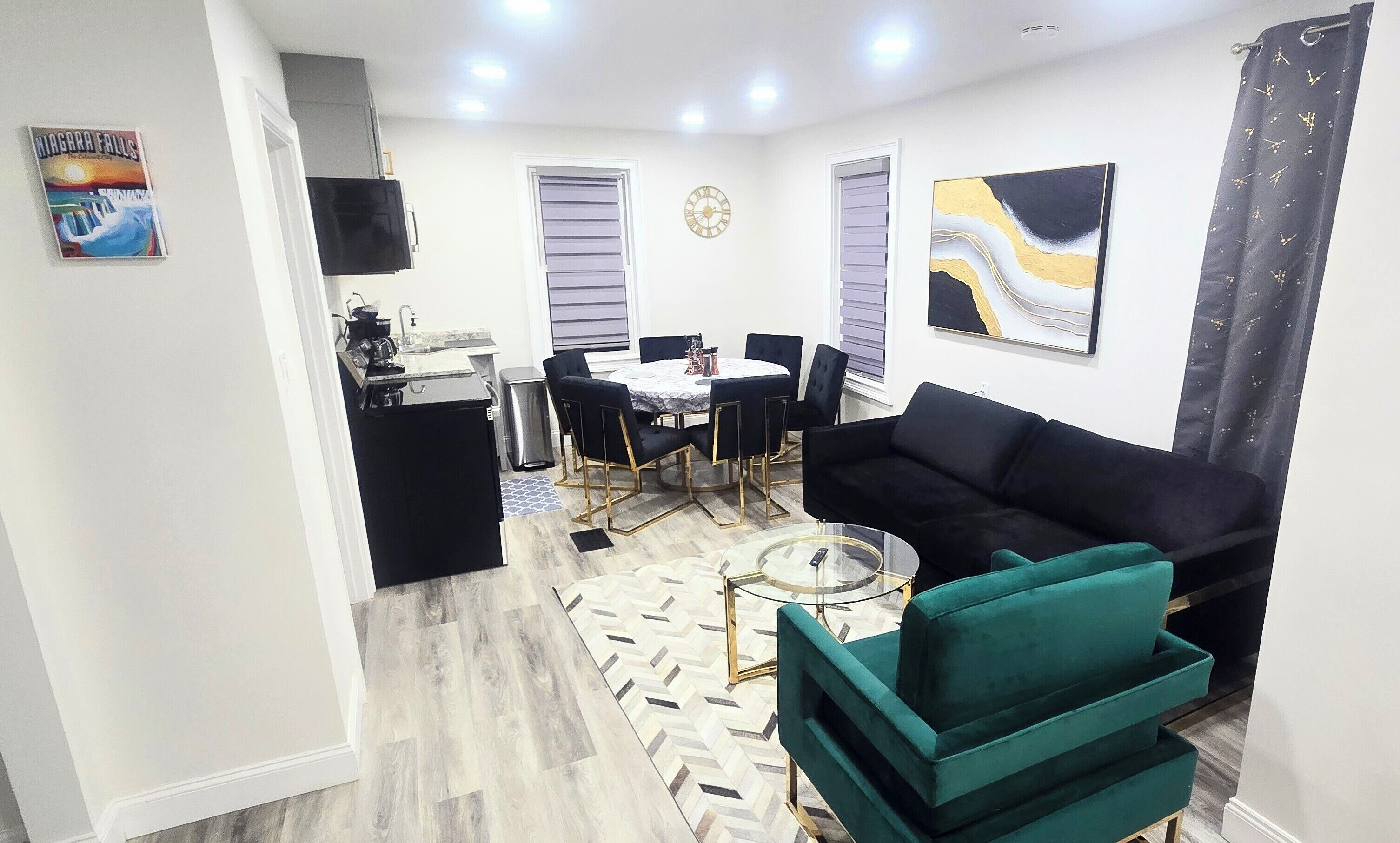 Una sala de estar moderna con un sofá negro, una mesa de centro de vidrio y un tapete con estampado de espiga.