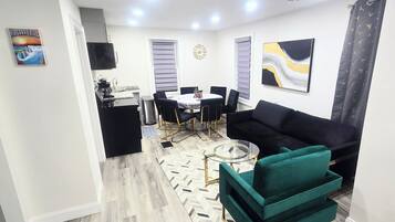 Una sala de estar moderna con un sofá negro, una mesa de centro de vidrio y un tapete con estampado de espiga.