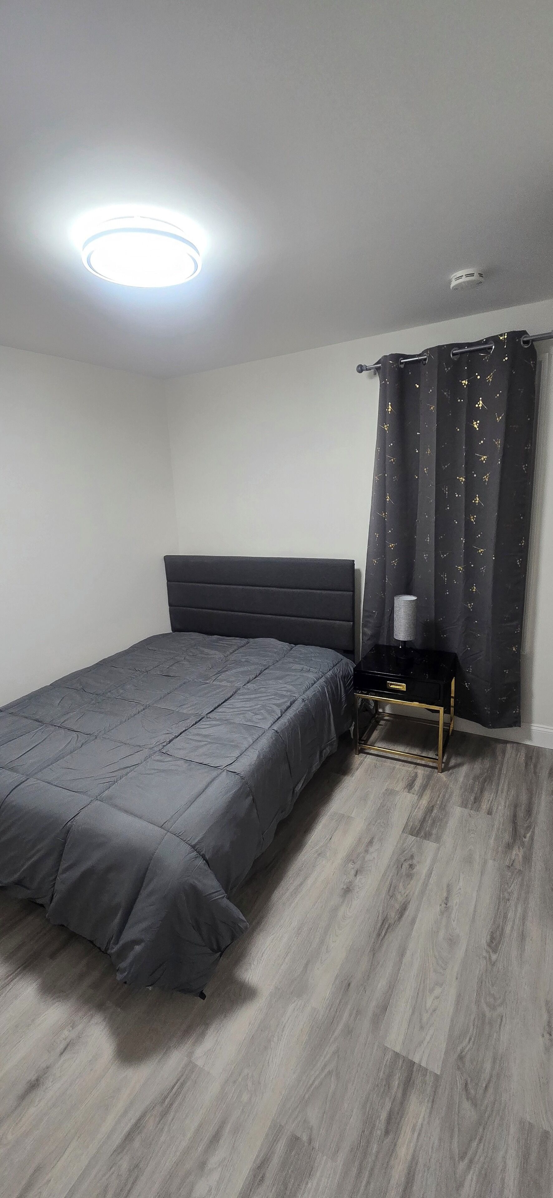 A bedroom with a bed, a nightstand, a lamp, and a window with curtains.