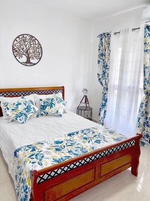 Cozy retreat with a comfortable bed, floral-patterned bedspread, and a decorative tree wall hanging.