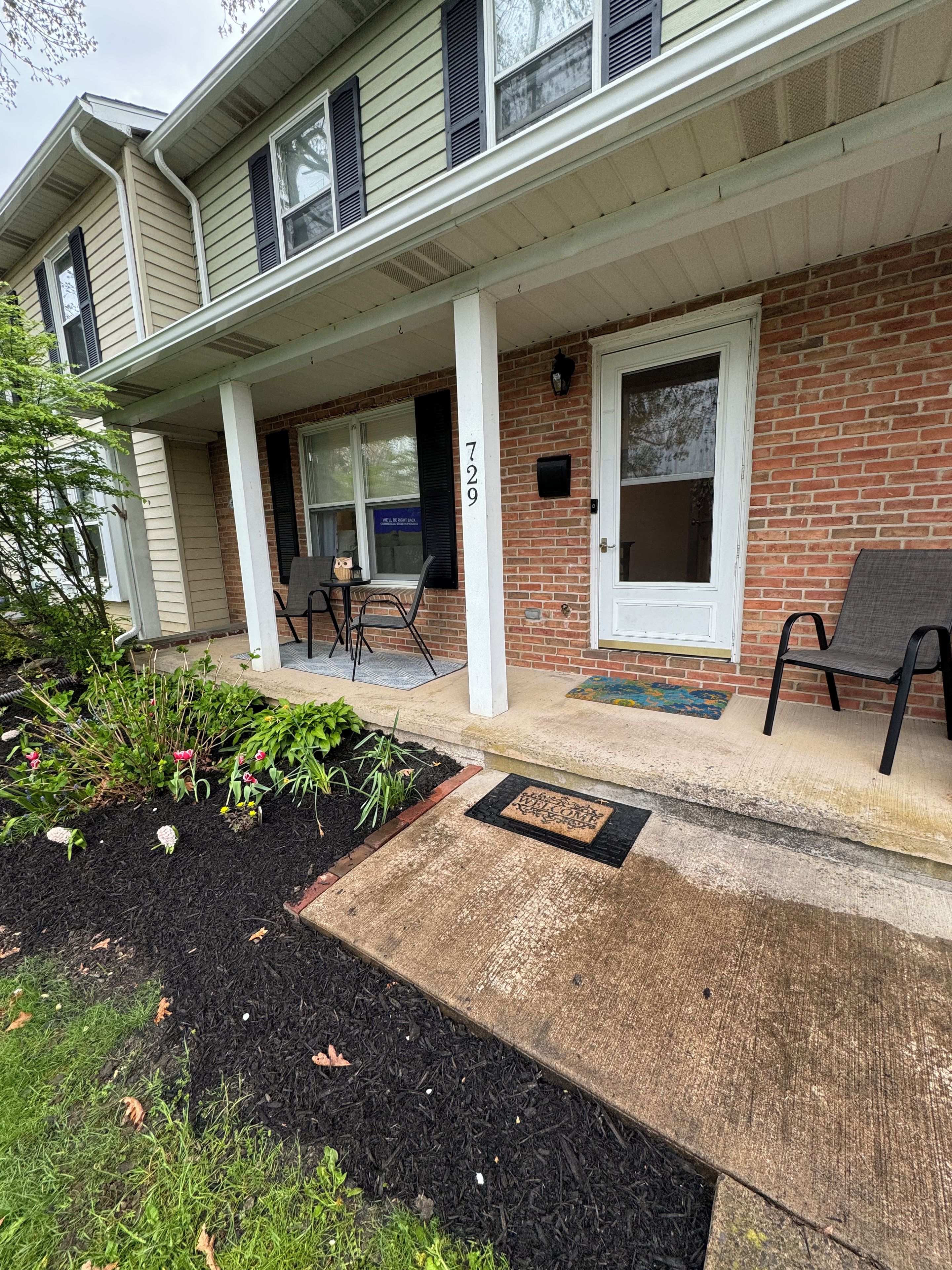 A two-story house with a brick facade, a front porch with a bench, and a mailbox.