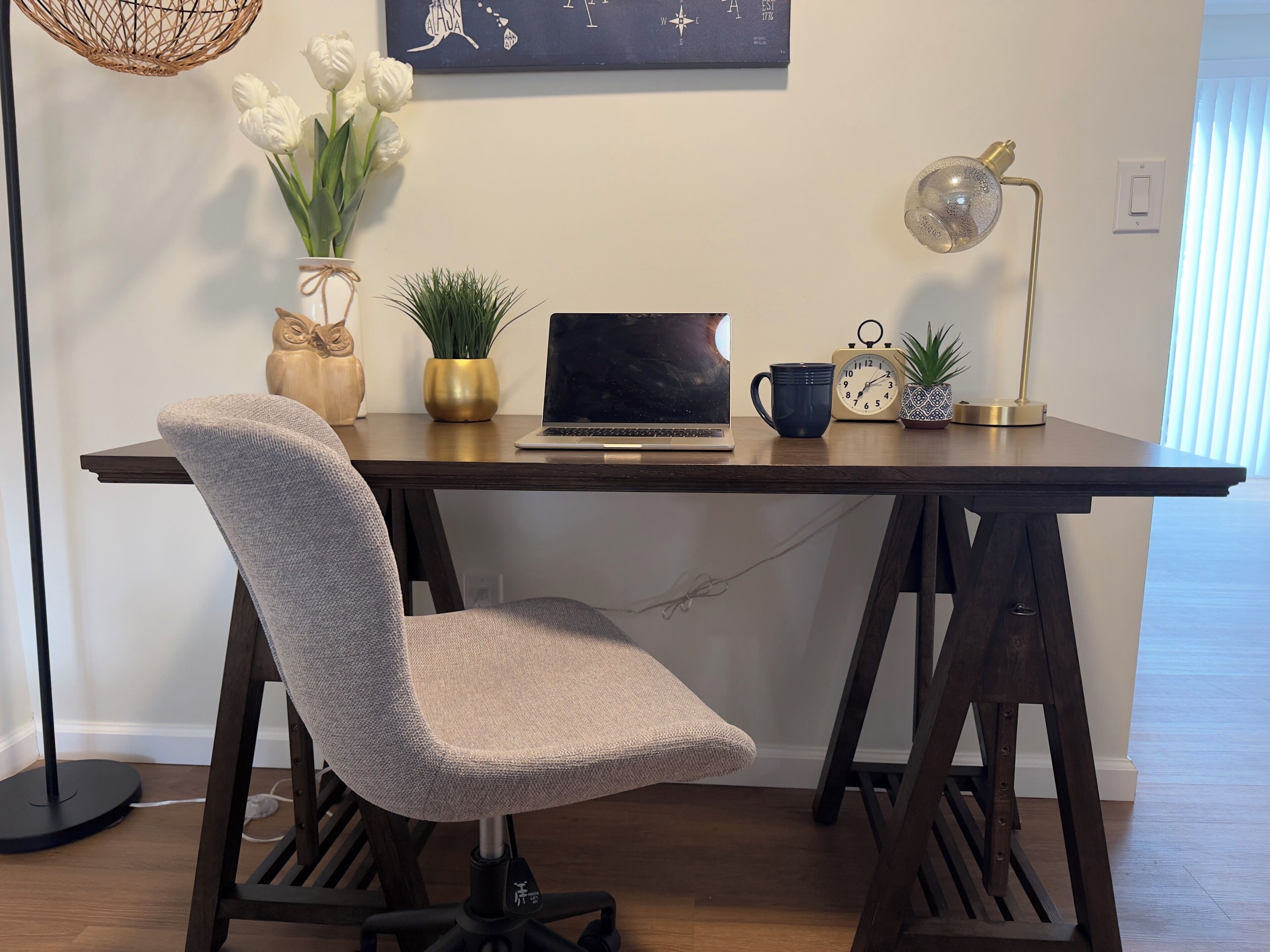 A modern workspace with a laptop, a clock, a coffee mug, and decorative plants on a wooden desk.