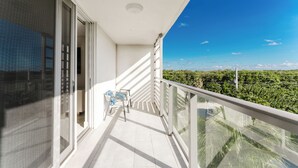 Un balcon donnant sur un paysage verdoyant, avec une balustrade blanche et une petite table entourée de chaises.