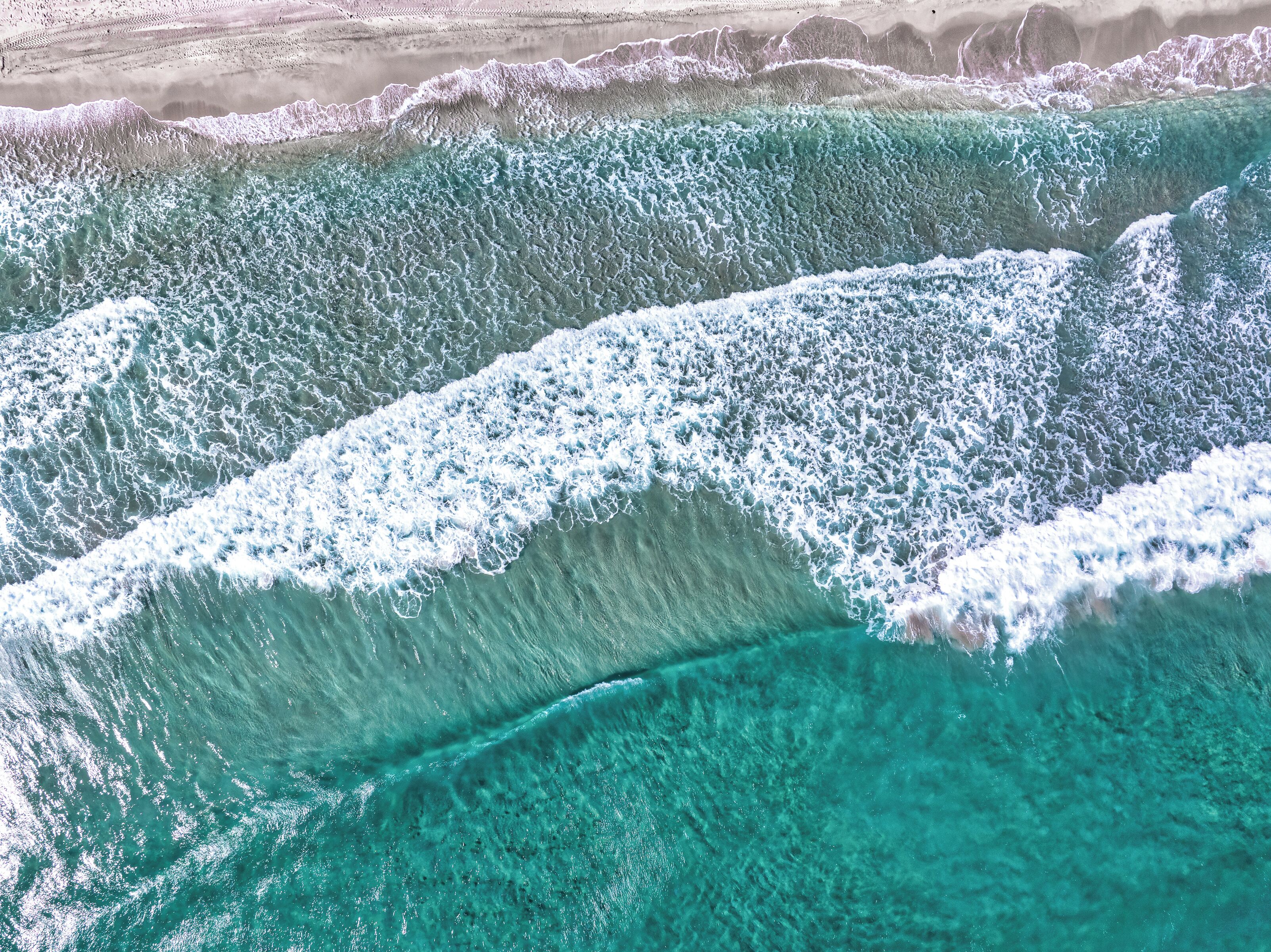 Ein Luftbild einer Strandlandschaft mit klarem türkisblauem Wasser und brechende Wellen.