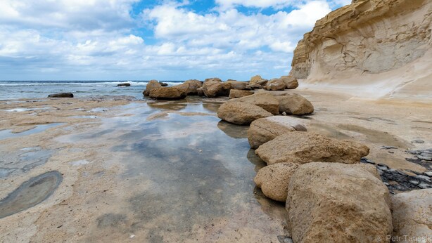Une plage rocheuse parsemée de gros blocs et bordée d’une falaise.
