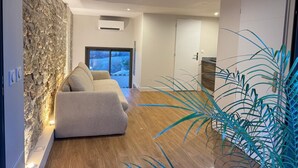 Un salon moderne avec un mur d’accent en pierre, un canapé et une vue dégagée sur l’extérieur grâce à une grande fenêtre.
