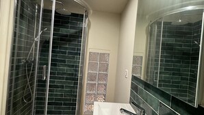 Une salle de bain moderne avec une douche à l’italienne aux lignes courbes, un grand miroir et une baignoire blanche.