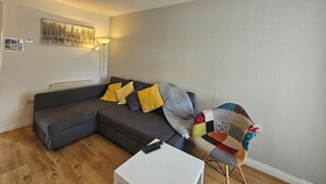Ein modernes Wohnzimmer mit einem grauen Ecksofa, einem weißen Couchtisch und einem farbenfrohen Sessel.