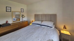 Ein Schlafzimmer mit einem großen Bett, einem Nachttisch, einem Spiegel und einem an der Wand befestigten Regal.