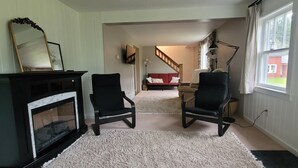 A living room with a fireplace, two black chairs, a red couch, and a staircase leading to another room. - The Homestead - modern beauty, spacious, private, super clean! (Chassell)