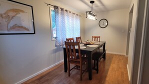 A dining area with a wooden table and chairs, a clock on the wall, and a window with curtains. - The Homestead - modern beauty, spacious, private, super clean! (Chassell)
