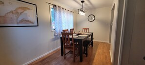 Un comedor con una mesa y sillas de madera, un reloj en la pared y una ventana con cortinas.