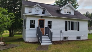 A two-story white house with a front porch, a compass decoration, and a small attached garage. - The Homestead - modern beauty, spacious, private, super clean! (Chassell)