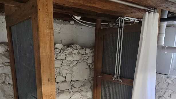 A rustic wooden bench under a slanted ceiling with a shower area, stone walls, and a metal pipe. - The Homestead - modern beauty, spacious, private, super clean! (Chassell)
